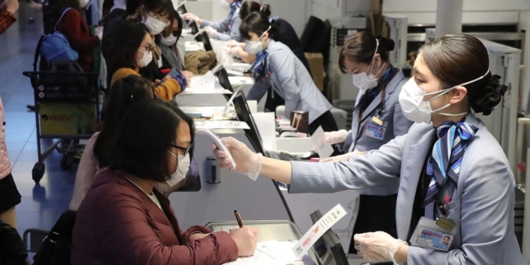 Chinese passengers are checked body temperature by staffs wearing mask and rubber glove at the Spring Airlines check-in counter to board an airplane bound for Wuhan at Haneda International Airport in Tokyo on January 31, 2020. The number of the patients who have been infected with a new coronavirus has reached to 9,692 and the death toll has been confirmed over 213 so far as of January 31th in China.   ( The Yomiuri Shimbun )